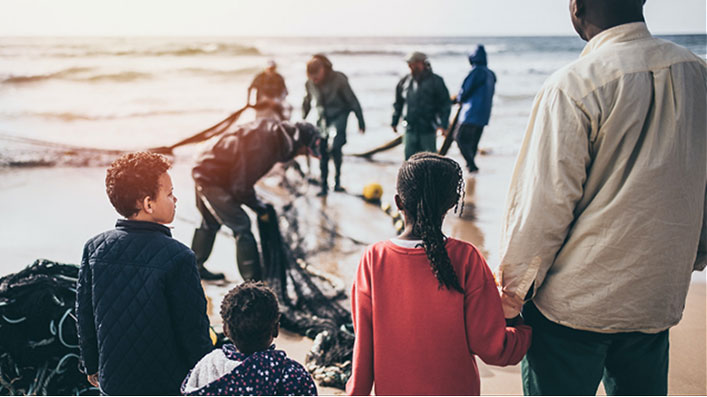 A father and his three children looking at the sea as fishermen gather a net