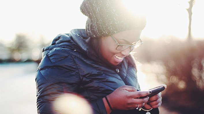 A Black woman looking at her cell phone and smiling