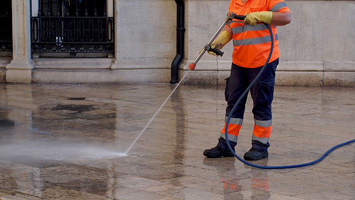 A public worker cleaning the street with a water hose