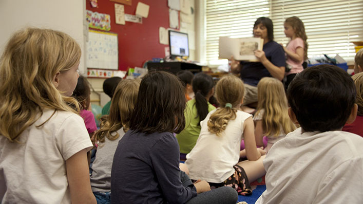 A teacher showing a book to a group of children in a kindergarten classroom