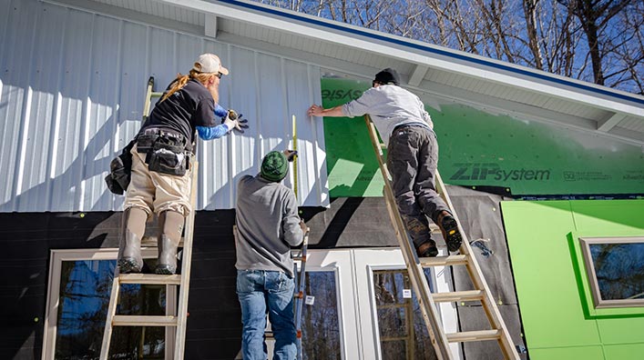 Three people on ladders refurbishing a house.
