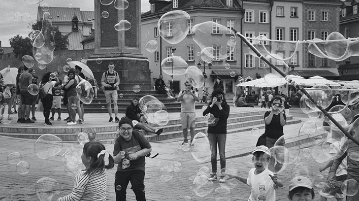 A group of children having fun and playing with soap bubbles in an open square.